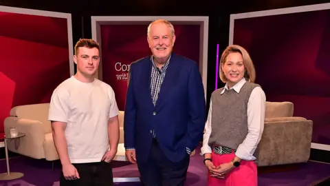 Pacemaker Press Three people standing beside each other, two men and a woman. The man has short dark hair and is wearing a white t-shirt. The man has short grey hair and is wearing a blue blazer and checked shirt. The woman has shoulder length blonde hair and is wearing pink trouser, white shirt and brown jumper.