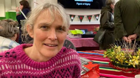 Rachel Vollerthun wears a pink Christmas jumper and there is festive bunting and flowers over her shoulder