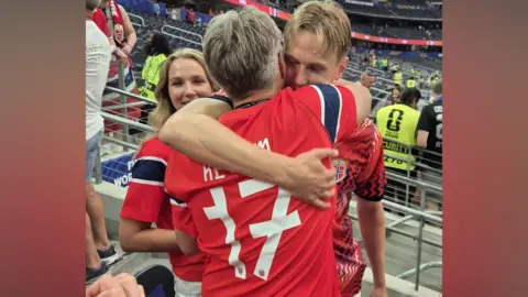 Supplied Two men in football jerseys hug inside a stadium