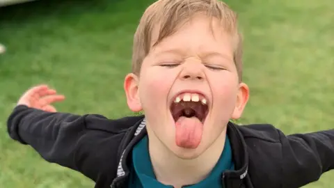 Family An eight-year-old boy with his arms outstretched behind him, his eyes squeezed shut and his tongue sticking out in a playful manner