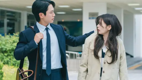 Netflix A scene from the Korean drama Love Next Door, where the hero grabs the heroine's coat as they both walk down the street. 