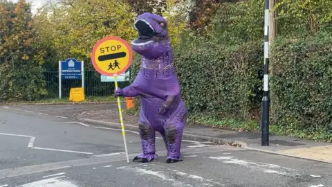 BBC Eight foot purple dinosaur on patrol helping children cross a road in Edith Weston, Rutland