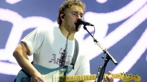 Sam Fender with his guitar in front of a neon sign