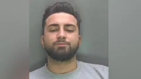 A mugshot of Razvan wearing a grey sweater and looking down rather than at the camera. He has dark brown hair in a smart hipster style, and a beard and moustache.