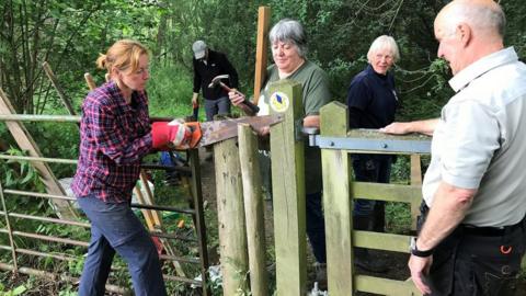 Five people working to repair a gate in the woods