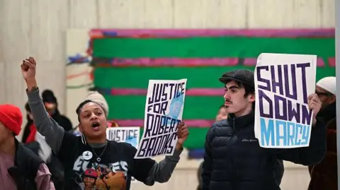 Protesters hold signs that read "justice for Robert Brooks"