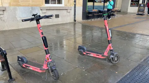 Two red Voi e-scooters parked on a street