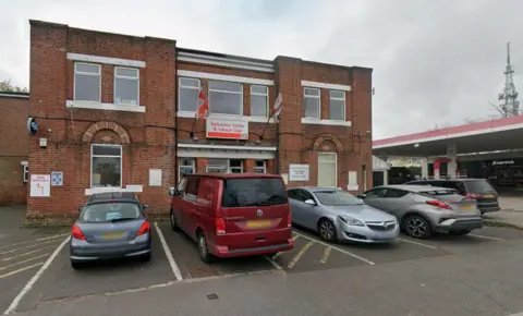 Outside the Parkstone Trades and Labour Club in Ashley Road in Poole on an overcast day. Several cars are parked in front of the building.
