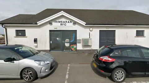 A white building with two cars parked in front of it. On the building it reads: Trimsaran RFC.
