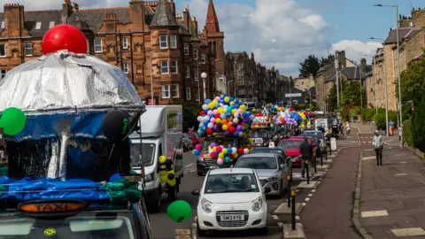 Mark Forsyth A parade of brightly coloured taxis travels down a residential street