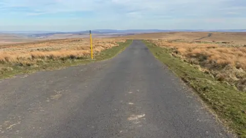Harry Byatt An empty moorland landscape is cut in two by a single well-maintained track road