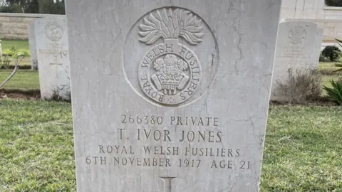 Adrian Hughes A white headstone in a cemetery with the inscription "T Ivor Jones, Royal Welsh Fusiliers" on it.