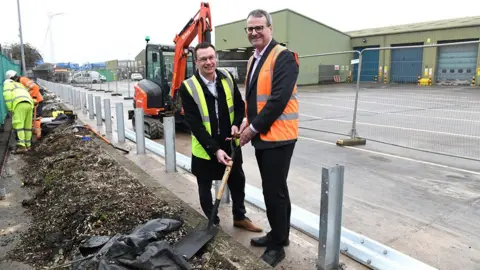 Stagecoach Two men in suits and high visibility jackets hold a spade at the site of the new bus depot