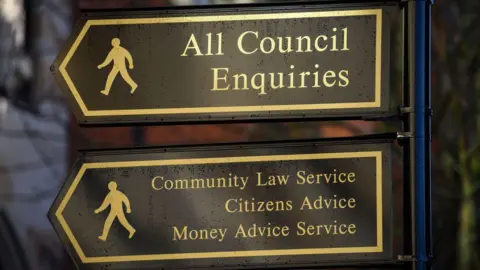 Getty Images Two black arrow signs, with gold writing. One says "all council enquires" and the other points to various services. There are also two silhouettes of men on each sign to symbolise walking.