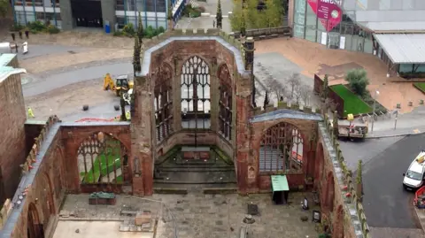 An aerial view of the ruins of the old Coventry Cathedral - it is roofless and the outer shell of the building remains standing.