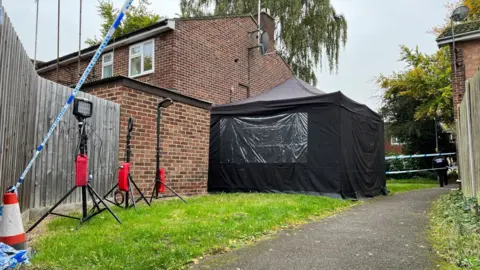 Stuart Woodward/BBC A black police tent and police cordon on Meadgate Avenue.