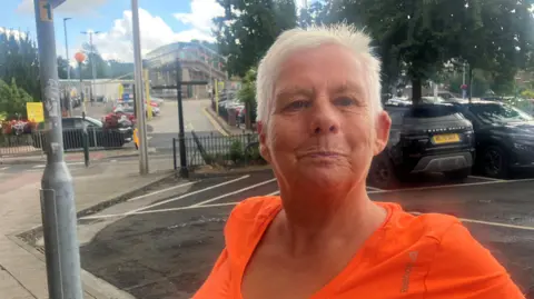 Photograph of Ellen Haslam from Macclesfield. She is pictured in the town centre, with the town's railway station in the background.