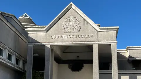 A court building with a coat of arms and the words Courts of Justice above the door.
