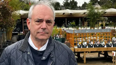 John Dipre stands at his garden centre wearing a quilted jacket