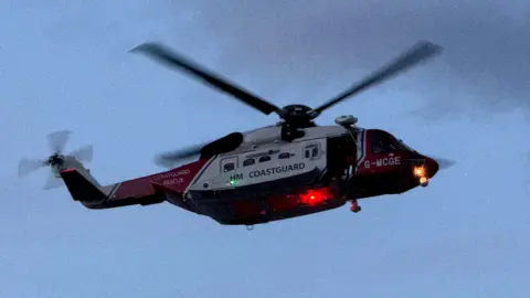 Phillip Norton/BBC A HM Coastguard helicopter in the skies over Hornsea. It is red and white and has lights on its undercarriage.