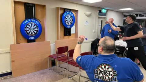 Two players at the Darts for All event throwing darts towards the Flexiboards, which allow people in wheelchairs to take part equally.