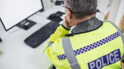 A traffic officer wearing a yellow his-vis jacket sat n front a computer screen 