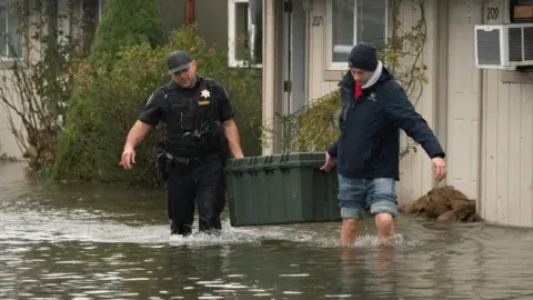 Deputy Sheriff Kalani Apilado helps Brandon Phasith carry belongings while evacuating amidst rising floodwater, as an atmospheric river brings rain and flooding to the Pacific Northwest, in Sultan, Washington