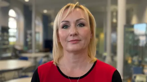 Councilwoman Beth Jones, who has blonde hair and is wearing a red and black dress. The background is blurred.