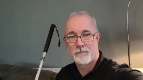 A head and shoulders shot of Julian Neale wearing glasses and holding a cane. 