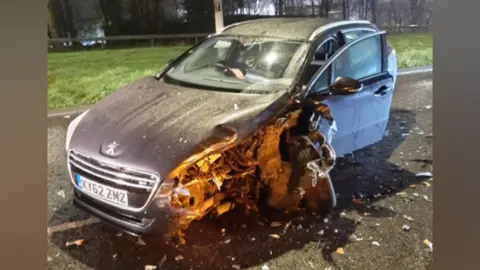 Thames Valley Police A grey car that has been involved in a collision. Part of its front and around the front left hand side tyre has been ripped off and destroyed in the crash. Debris rests on the road around the vehicle.