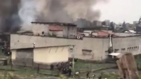 Black smoke billows from the prison's building as people flee from inside