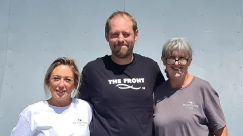 Stuart Welstead stands with two female members of staff on one of the skate ramps at the skatepark
