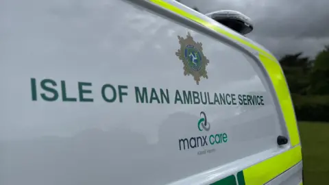 Isle of Man Ambulance Service in green block letters on the side of a Manx Care ambulance.