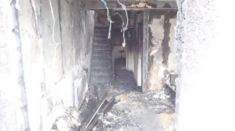 London Fire Brigade/X Interior of the house after the fire - the staircase is now burnt timbers and the floor is covered in ash and debris. 