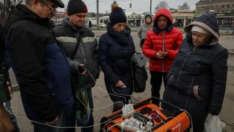 Reuters Local residents charge their phones powered by a generator at a street during a power outage after critical civil infrastructure was hit by Russian missile attacks, as Russia's invasion of Ukraine continues, in Kharkiv, Ukraine March 9, 2023