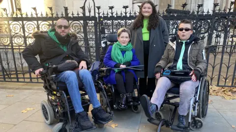BBC Claddag campaigners outside the Royal Courts of Justice. Adam Gabsi left, sitting in his mobility scooter. Sarah Rennie, centre, sitting in her mobility scooter. Georgie Hulme, right, sitting in her mobility scooter outside the High Court.