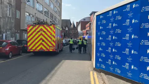 A fire engine parked outside a hospital. Three police officers carrying black bags can also be seen in the photo.