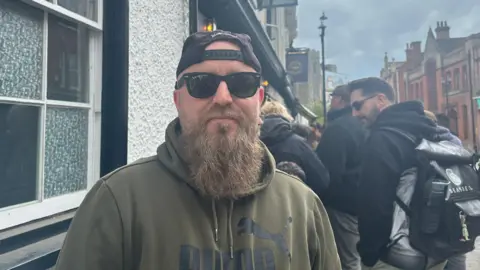 Aimee Dexter/BBC Michael Marron wears cap on head, has a beard and is sporting dark sunglasses. He is wearing a khaki sweatshirt.