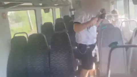 Man with face blurred and arms raised inside of train carriage