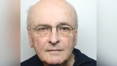 A police mugshot of Edward Phillips-Smith, a bald man wearing glasses. He is standing against a white backdrop.