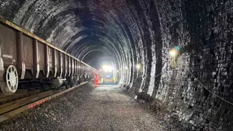 Track renewal work taking place inside a tunnel with a man in orange high viz near machinery