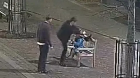 CCTV of two men vandalising a Paddinton Bear statue on a bench at night