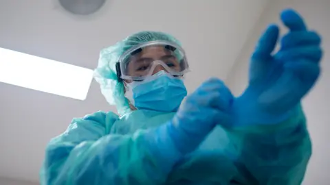 A female surgeon dressed in full blue hospital scrubs, surgical mask and gloves, prepares for an operation