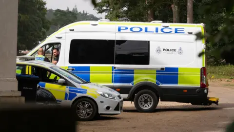 Shaun Whitmore/BBC A large police van and a police car parked next to each other. Two officers - including one in the passenger seat and one standing outside - talking