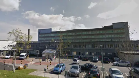 Google Prince Charles Hospital in Merthyr Tydfil - a large building with several storeys, and with vehicles in a car park at the front