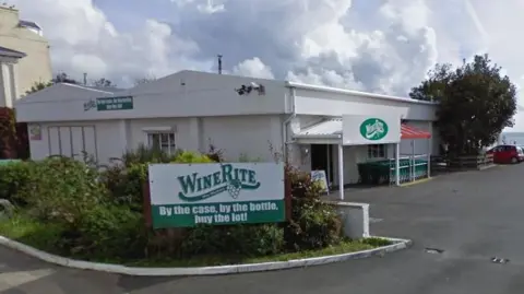 Google The exterior of Winerite, which is a large white building with a car park in front and a white and green sign that reads WineRite - By the case, by the bottle, buy the lot.