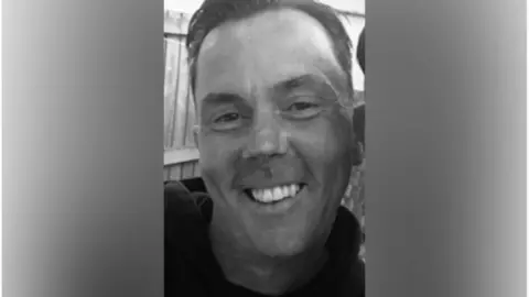 Kevin Thorne is seen from his shoulders up, smiling at the camera. The photo is in black and white.