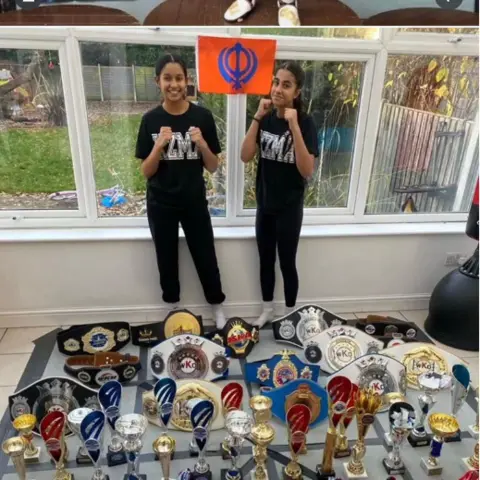 Family Dheep and Simran dressed all in black stood in front of lots of belts and trophies in a conservatory