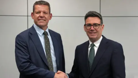 A formal picture of Rhun ap Iorwerth and Andy Burnham shaking hands