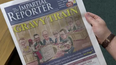 A copy of the Impartial Reporter with the headline 'Gravy Train' and an cartoon depiction of inside the council chamber. 